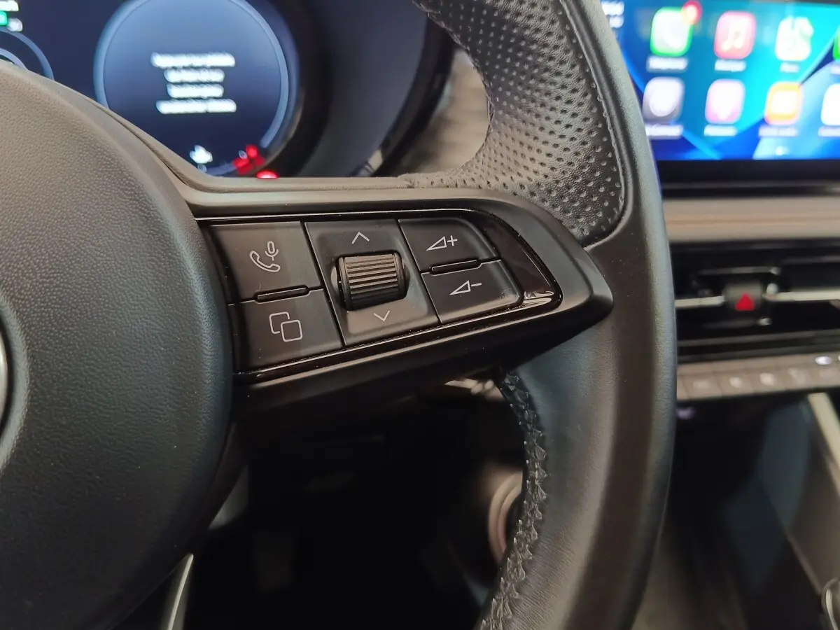 Gros plan sur les commandes gauche du volant cuir de l'Alfa Romeo Tonale 1.5T Hybrid 160 VGT, intérieur moderne.