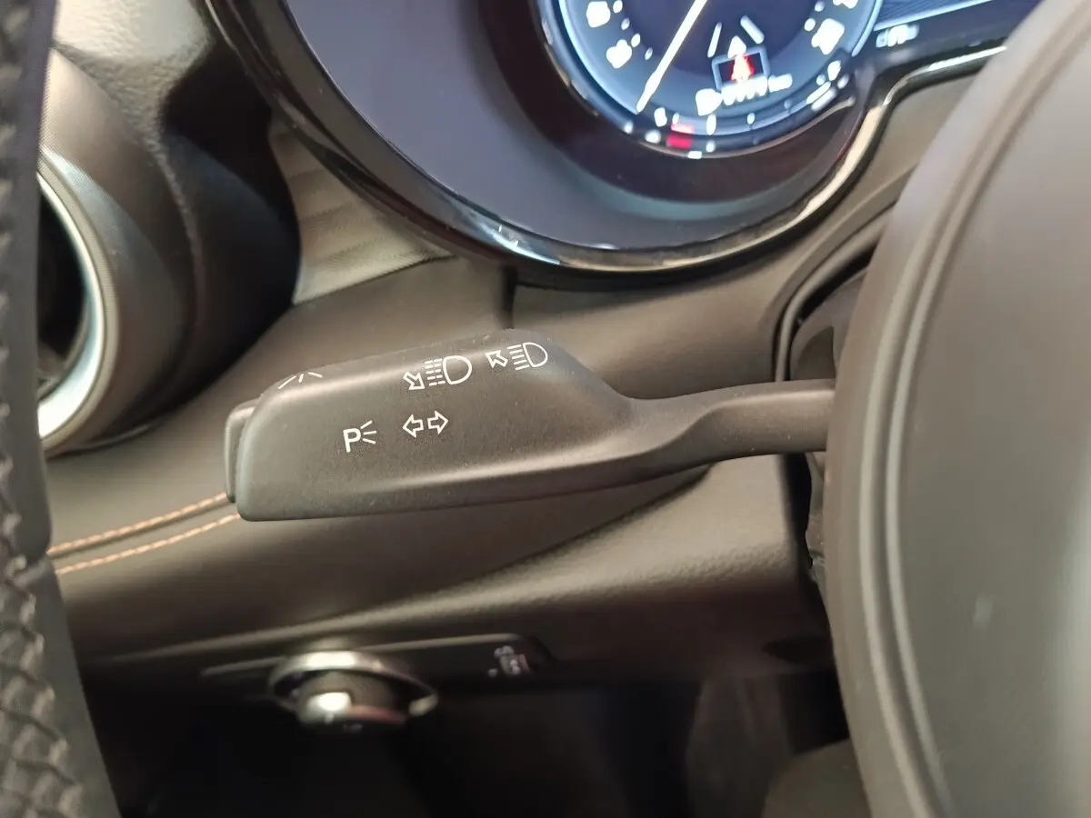 Gros plan sur la commande des clignotants et feux à gauche du volant dans l’habitacle noir de l’Alfa Romeo Tonale.