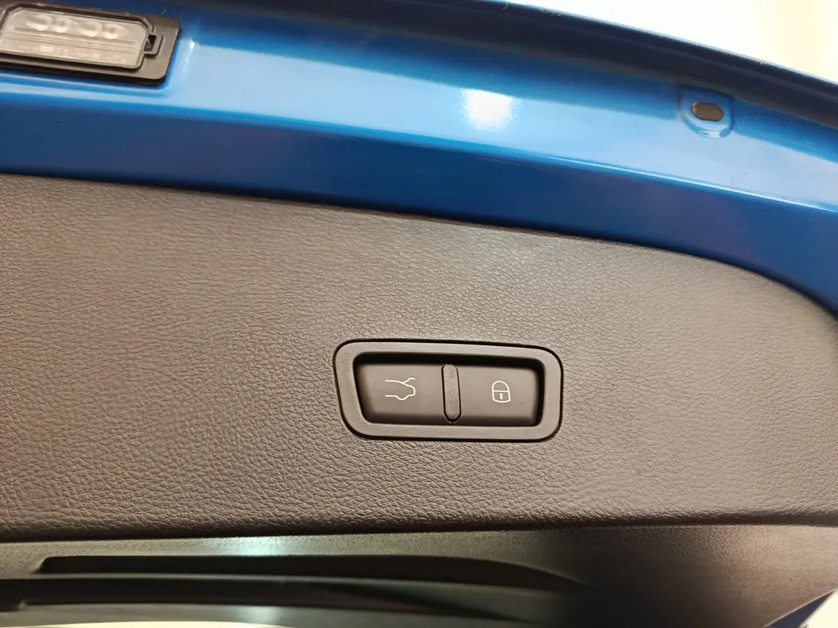 Gros plan sur la commande de fermeture électrique du coffre, entourée de la peinture bleue du hayon arrière.