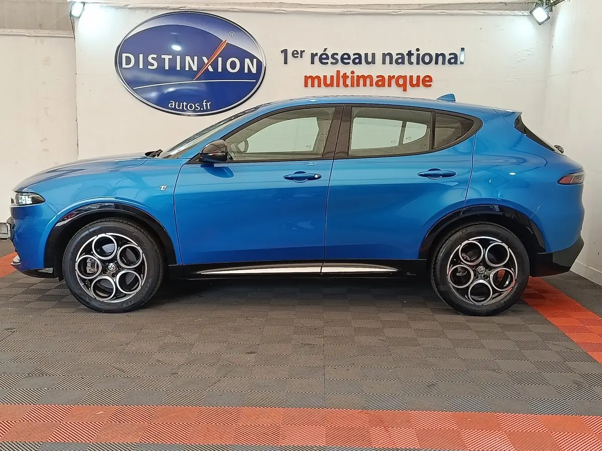 Vue de profil côté gauche d'Alfa Romeo Tonale 1.5T Hybrid 160 VGT bleu avec jantes distinctives en intérieur showroom.