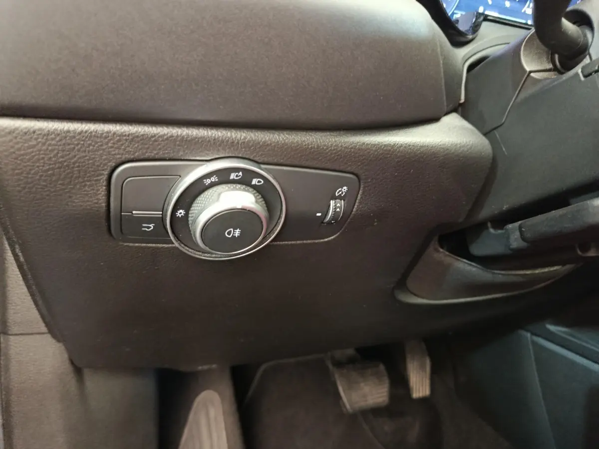 Gros plan sur le bouton de commande des phares noir à gauche du volant dans l’habitacle de l’Alfa Romeo Tonale 2023.