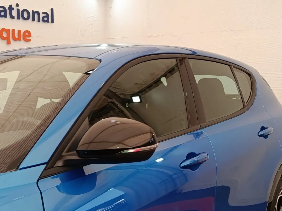 Vue latérale gauche rapprochée de l'Alfa Romeo Tonale bleu avec rétroviseur noir et poignées de porte assorties.