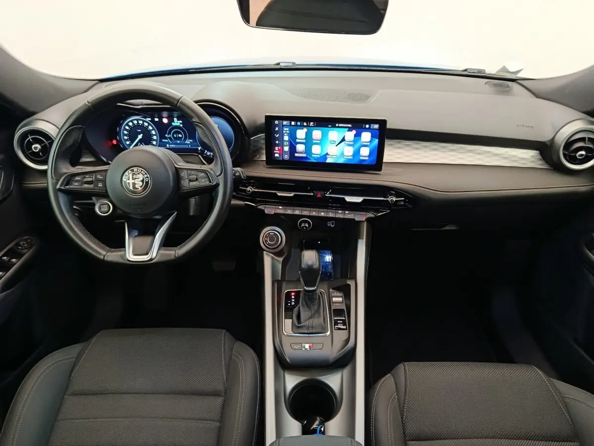 Vue intérieure avant de l'Alfa Romeo Tonale 1.5T Hybrid 2023, tableau de bord noir avec écran tactile central et volant cuir.