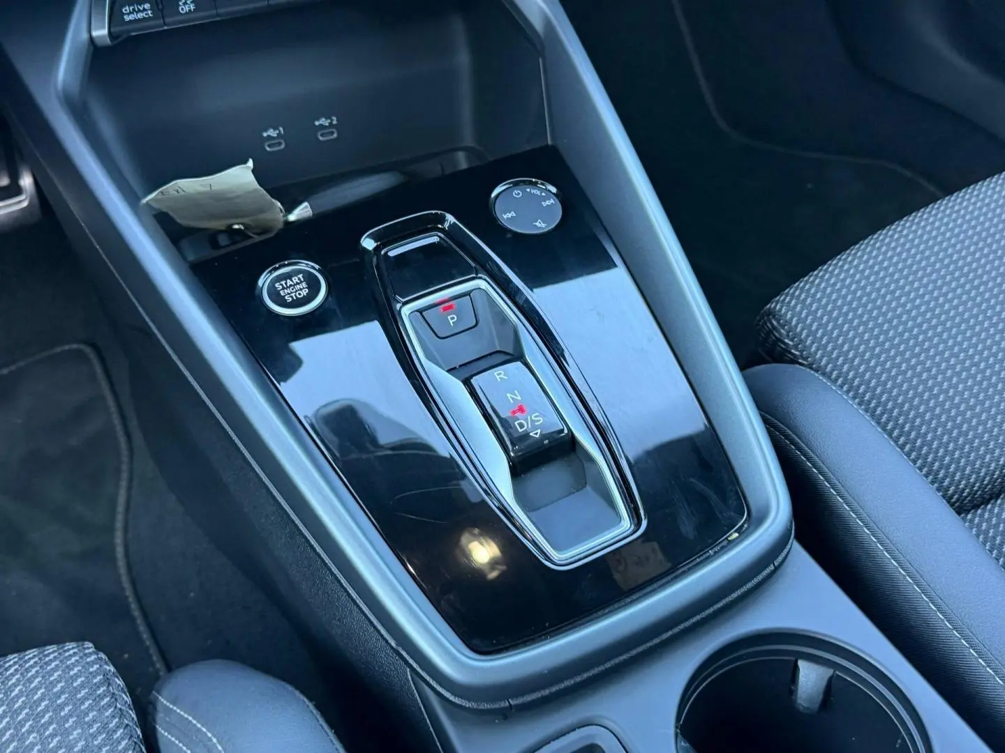 Vue rapprochée de la console centrale noire brillante avec levier de vitesses automatique et bouton Start/Stop dans un Audi A3 Sportback noir Mythic.