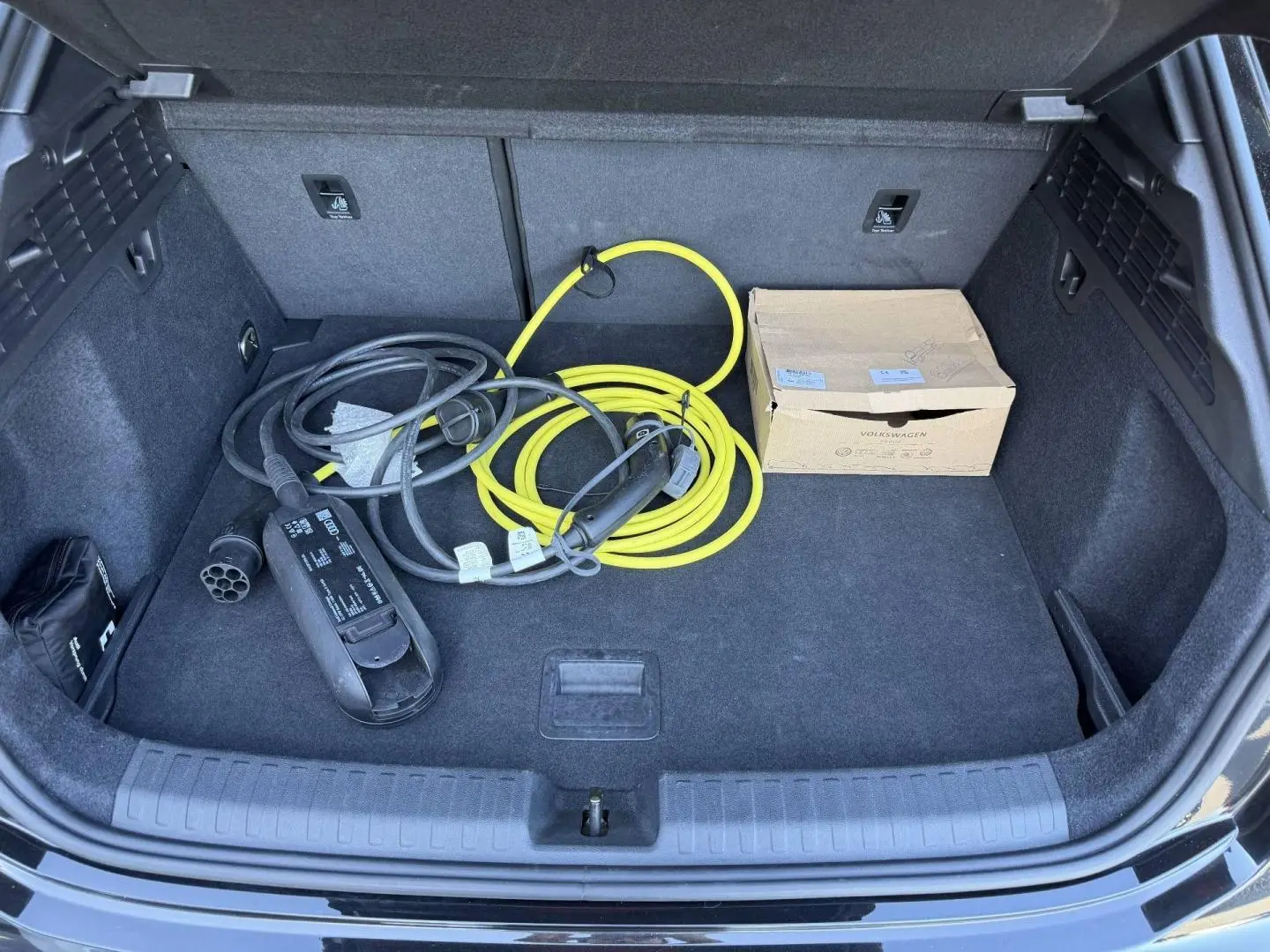 Coffre ouvert d'Audi A3 Sportback 2025 noir Mythic avec câbles de recharge hybride et carton Volkswagen.