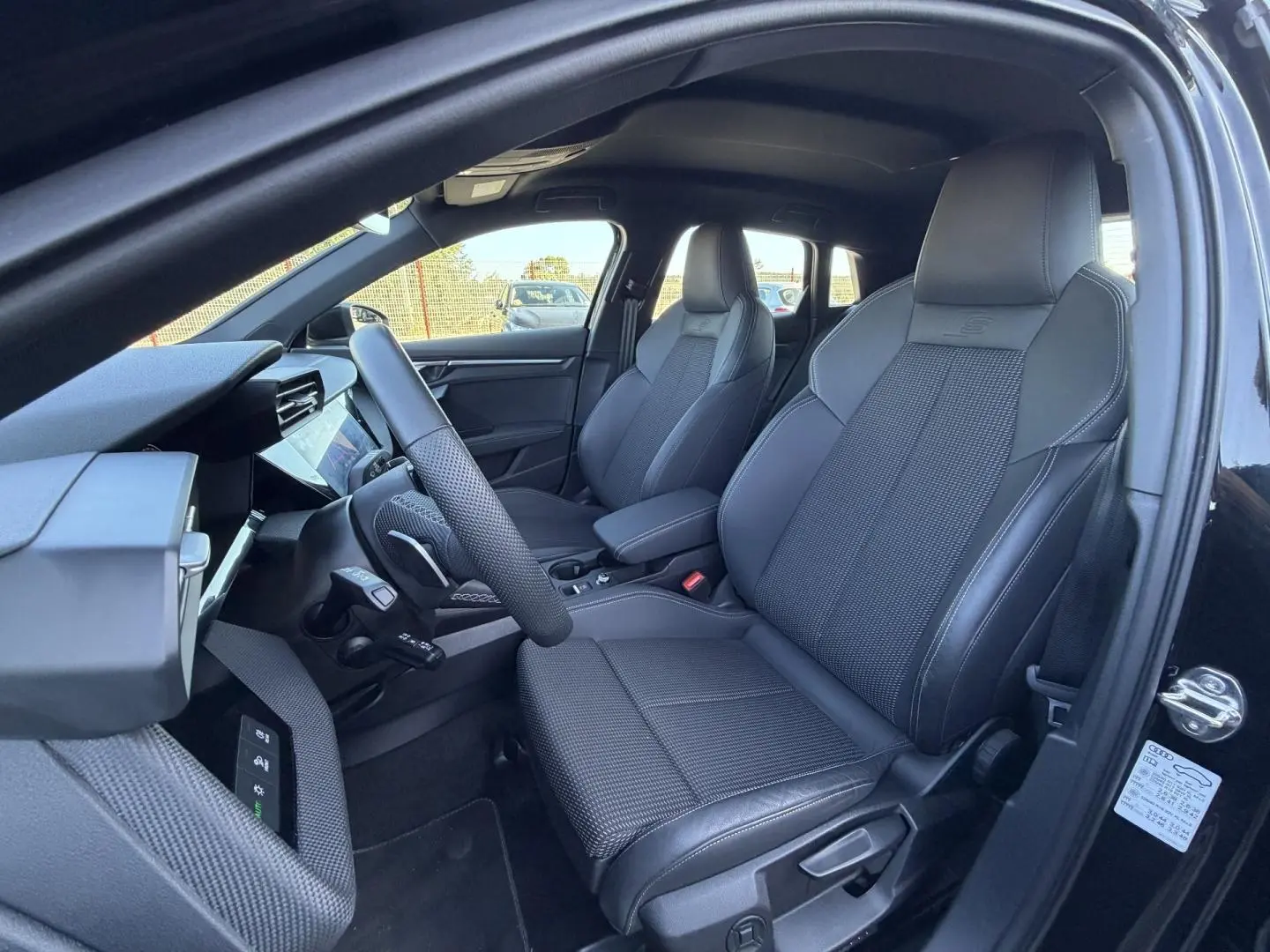 Vue intérieure côté conducteur de l'Audi A3 Sportback 2025 noir Mythic, sièges sport en cuir et tissu avec logo S embossé.