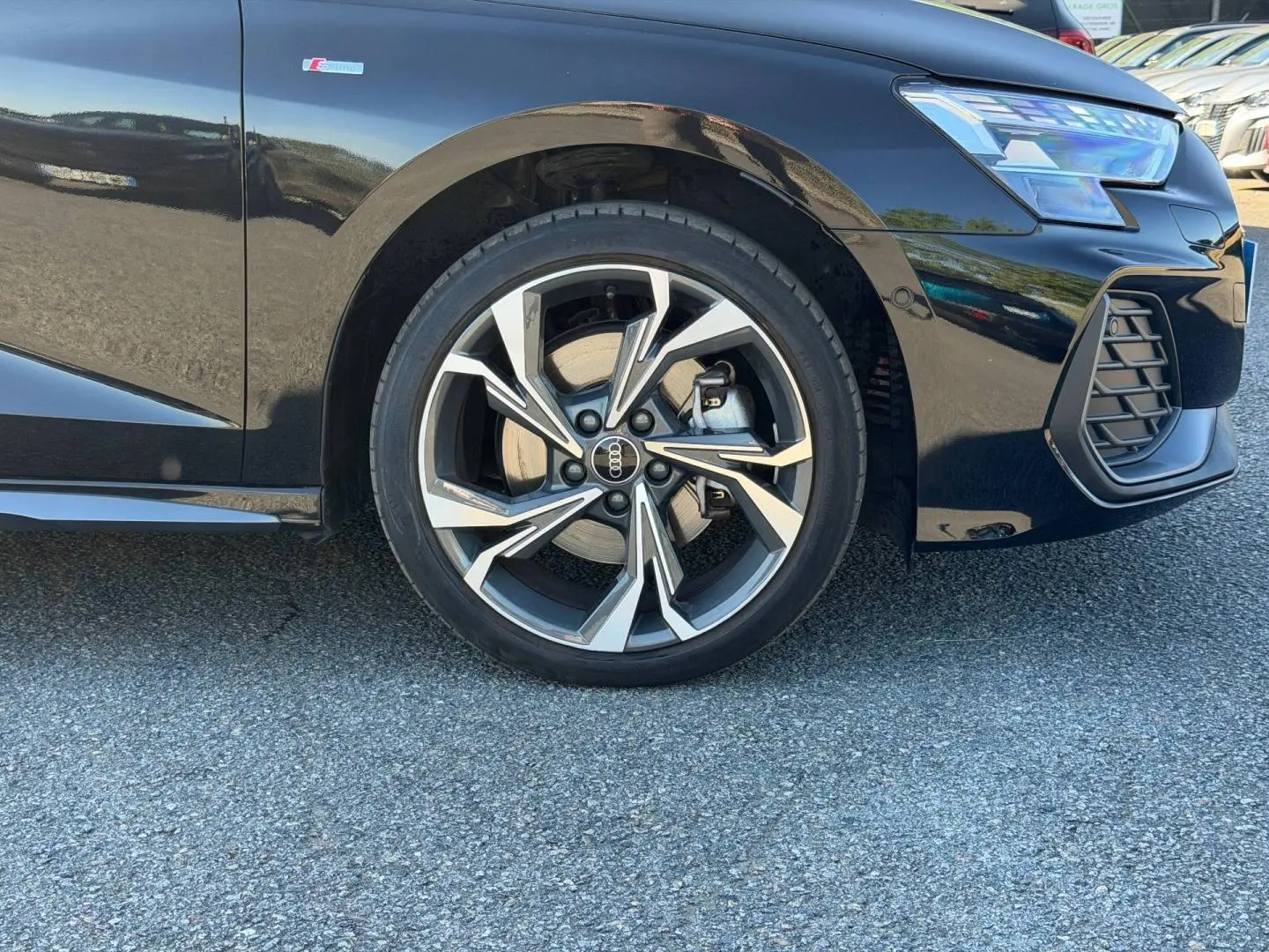 Gros plan sur la roue avant droite et le pare-chocs avant d’une Audi A3 Sportback noir Mythic métallisé avec jante alu distinctive.