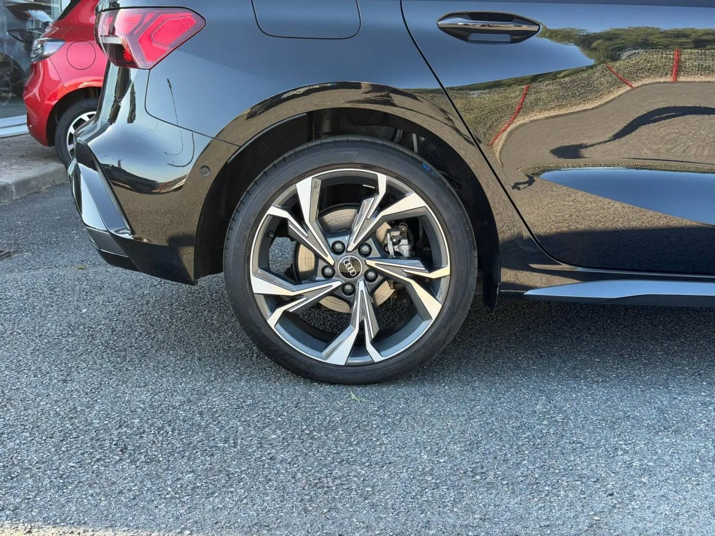 Gros plan sur la roue arrière droite d’une Audi A3 Sportback noire Mythic métallisée avec jante alu distinctive.