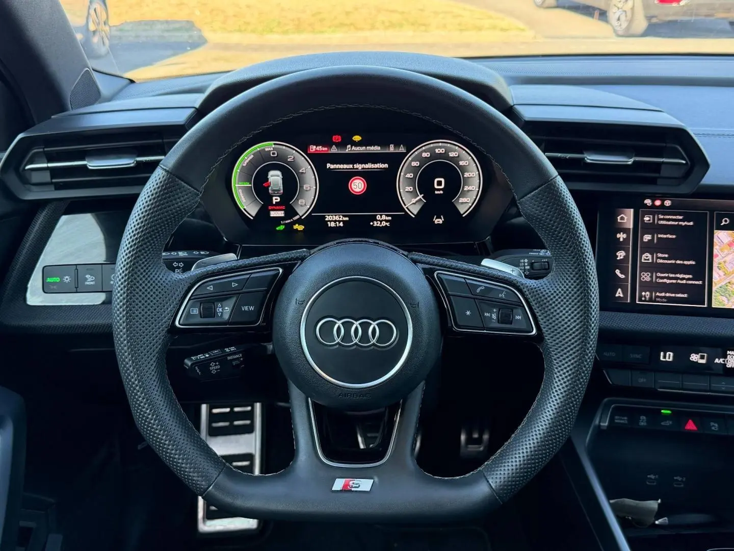 Vue intérieure centrée sur le volant sport Audi S avec tableau de bord numérique et écran tactile à droite.