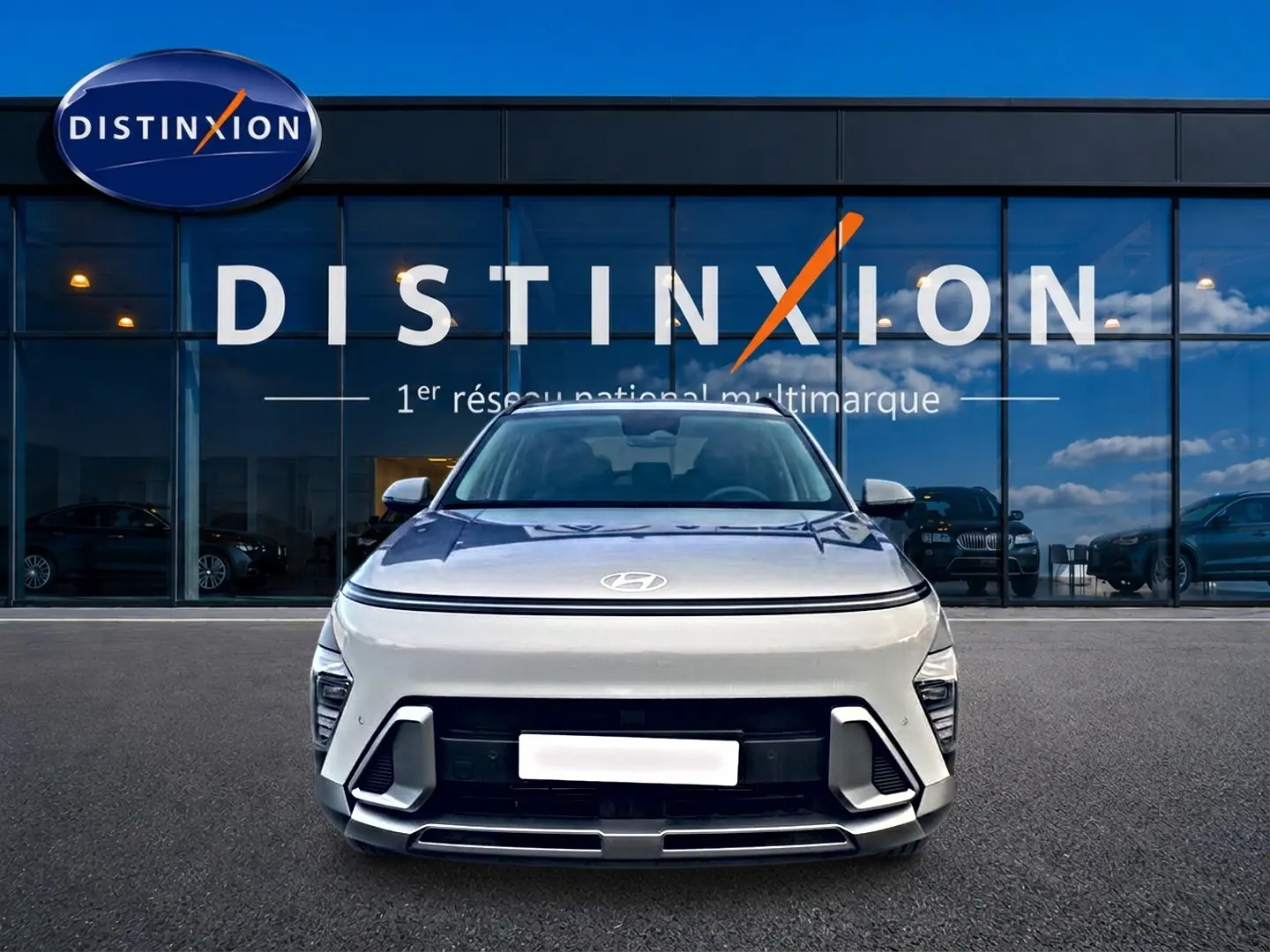 Vue frontale d'un Hyundai Kona gris 2025 avec calandre moderne et feux LED intégrés, devant une vitrine Distinxion.