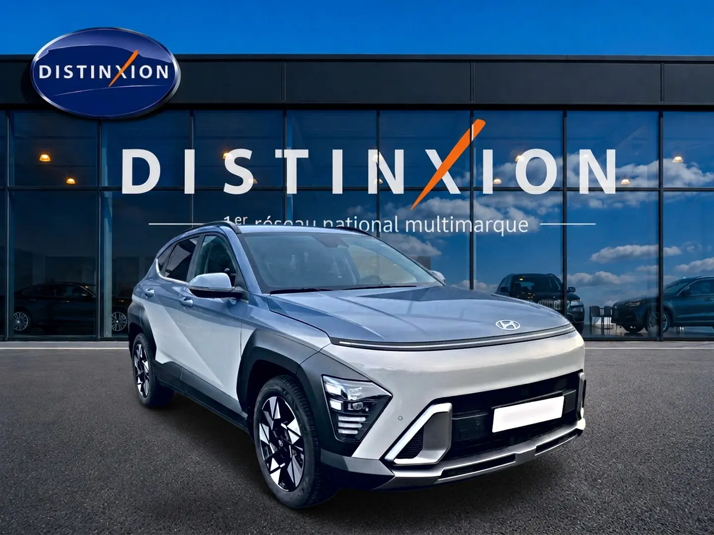 Vue 3/4 avant droit d'un Hyundai Kona gris clair avec jantes alliage et calandre au design futuriste devant un showroom Distinxion.