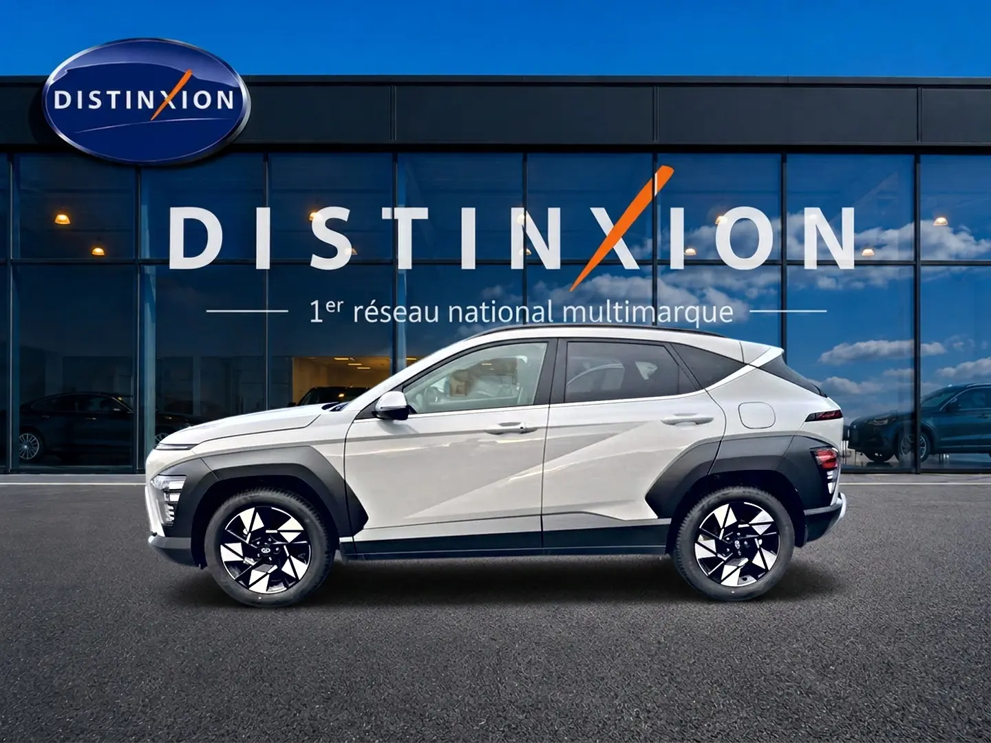 Vue latérale droite d'un Hyundai Kona gris 2025 avec protections noires et jantes alliage bicolores devant une vitrine Distinxion.