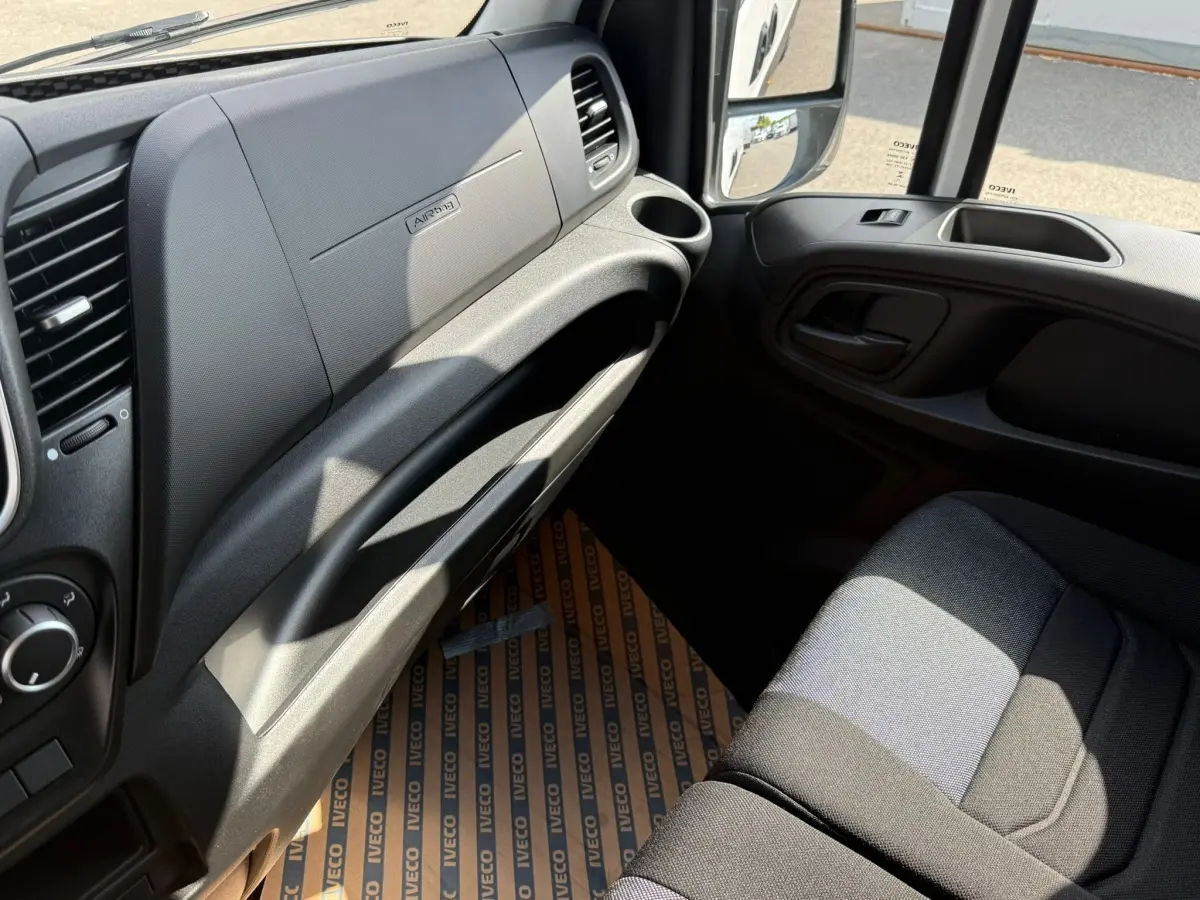 Vue intérieure côté passager du tableau de bord et siège gris foncé du fourgon Iveco Daily blanc, avec porte ouverte.