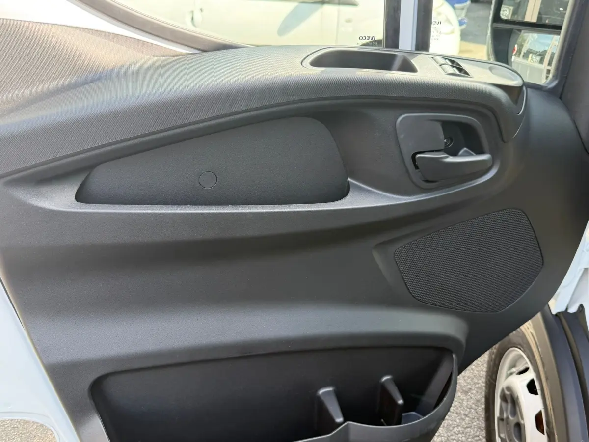 Vue rapprochée de la porte côté droit du fourgon Iveco Daily blanc, montrant la poignée intérieure et le haut-parleur intégré.