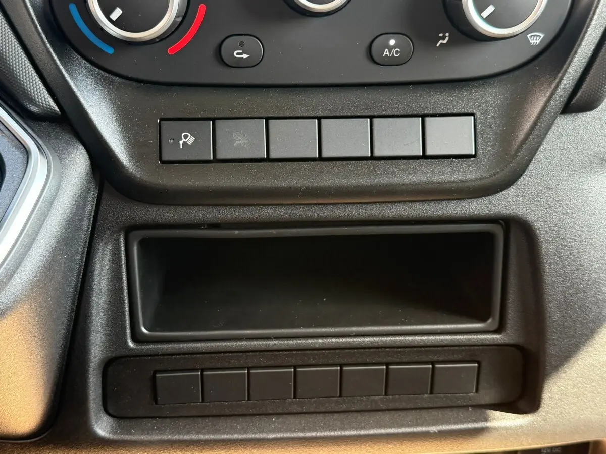 Gros plan sur la console centrale noire de l’IVECO Daily 35S18, montrant les commandes de climatisation et rangements.