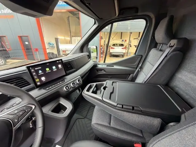 Vue intérieure côté passager du Renault Master 2025 gris urbain, avec banquette et bureau mobile déployé.