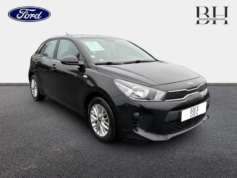KIA Rio noir Ébène vue 3/4 avant droit, avec calandre chromée et jantes alu visibles.