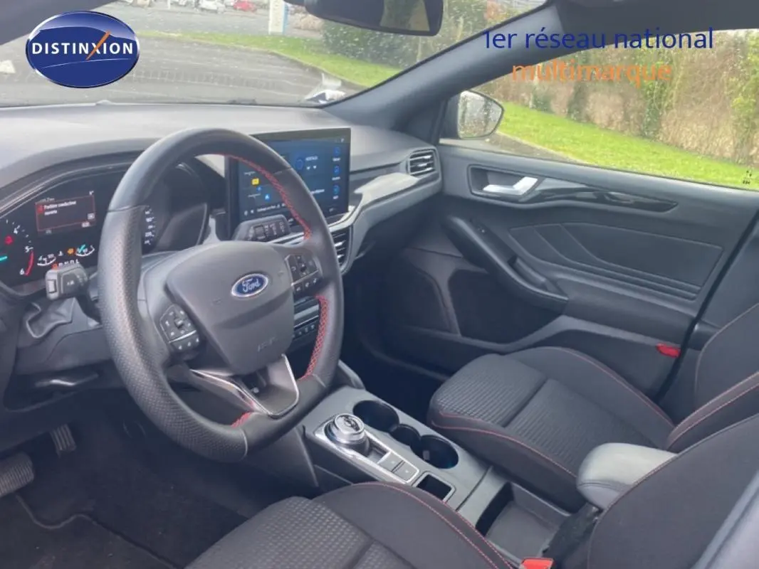 Vue intérieure côté conducteur de la Ford Focus 2024 gris foncé, avec volant sport, écran tactile et accoudoir central.