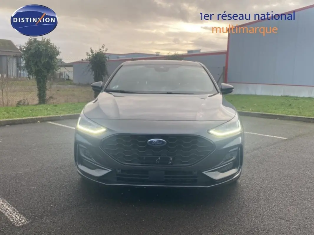 Vue avant d'une Ford Focus 1.5 EcoBlue gris foncé avec phares LED allumés sur parking extérieur.
