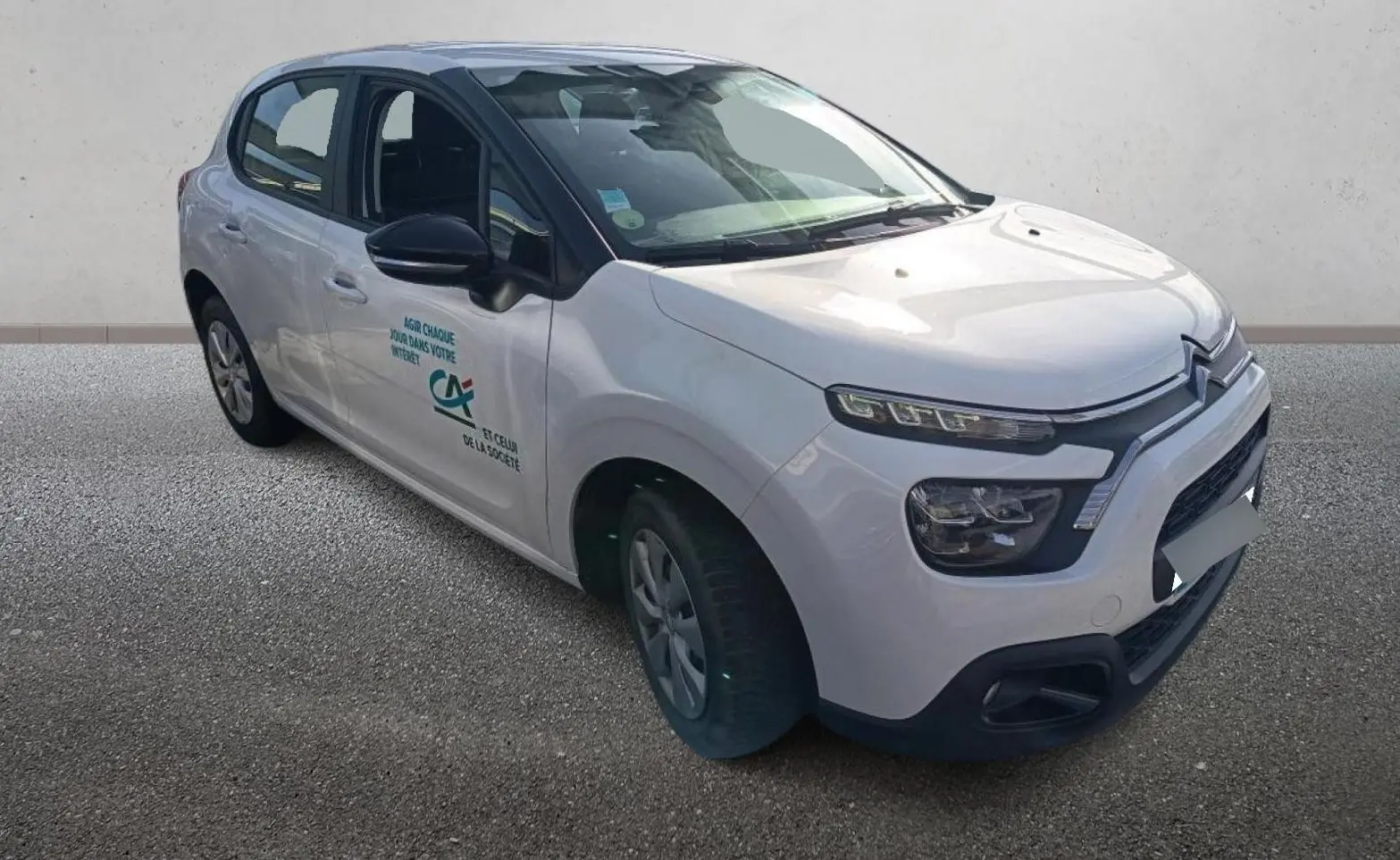Citroën C3 blanche vue 3/4 avant droit avec logo Crédit Agricole sur la porte avant.