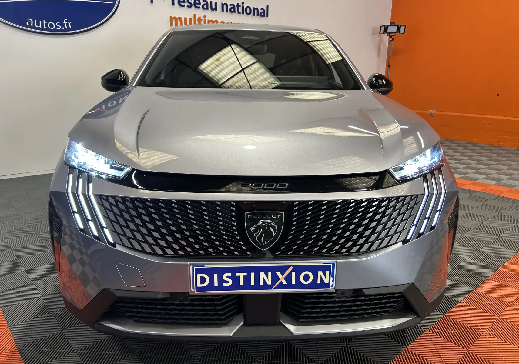 Vue frontale du Peugeot 3008 III Hybrid gris Artense avec calandre noire et feux LED verticaux allumés.