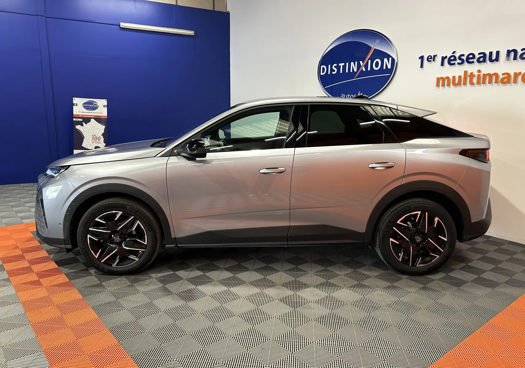 Vue latérale droite du Peugeot 3008 III Hybrid gris Artense avec jantes noires et toit noir dans un showroom.