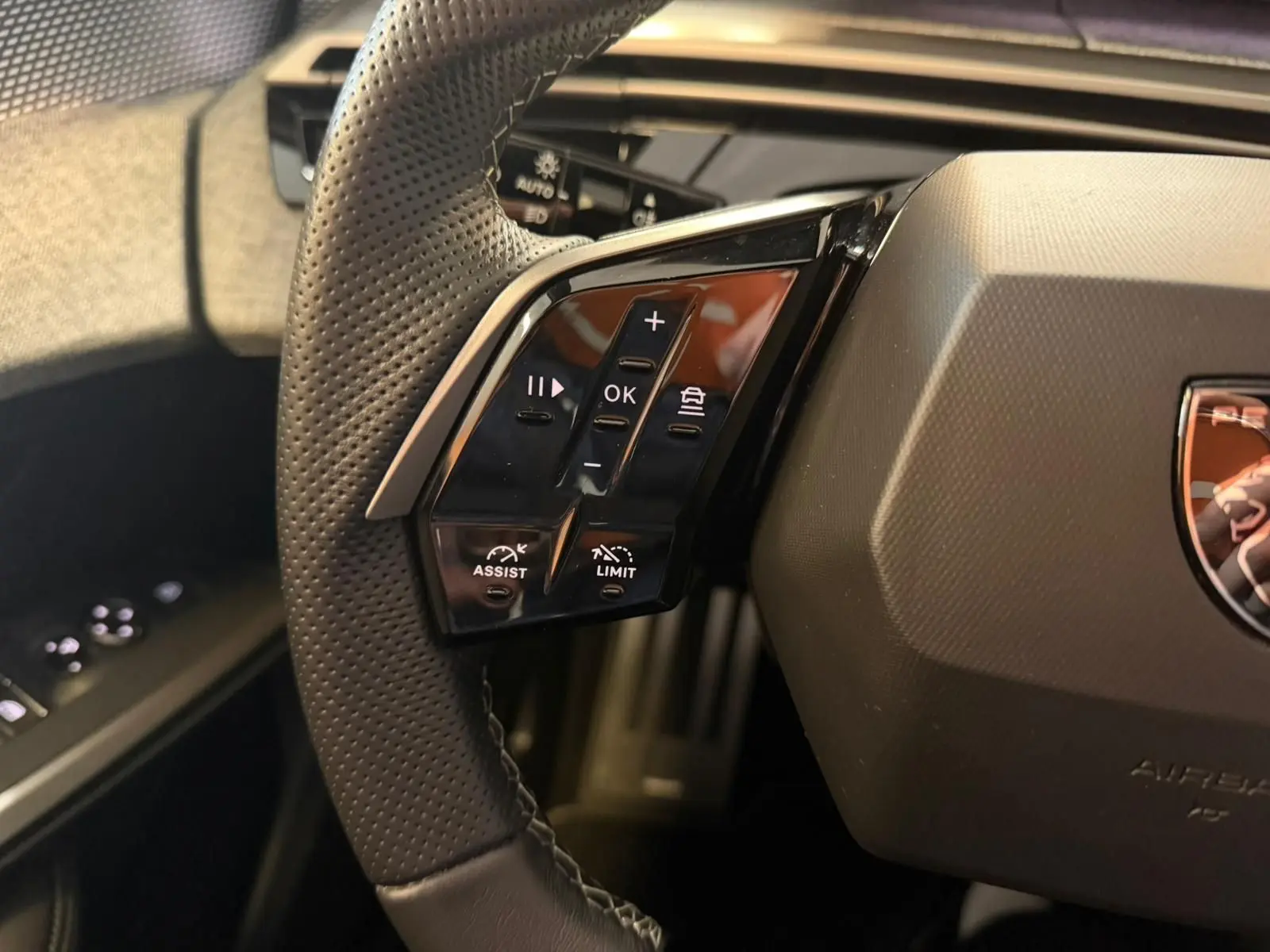 Gros plan sur les commandes gauche du volant perforé du Peugeot 5008 Hybrid 145 e-DCS6 GT, intérieur noir.