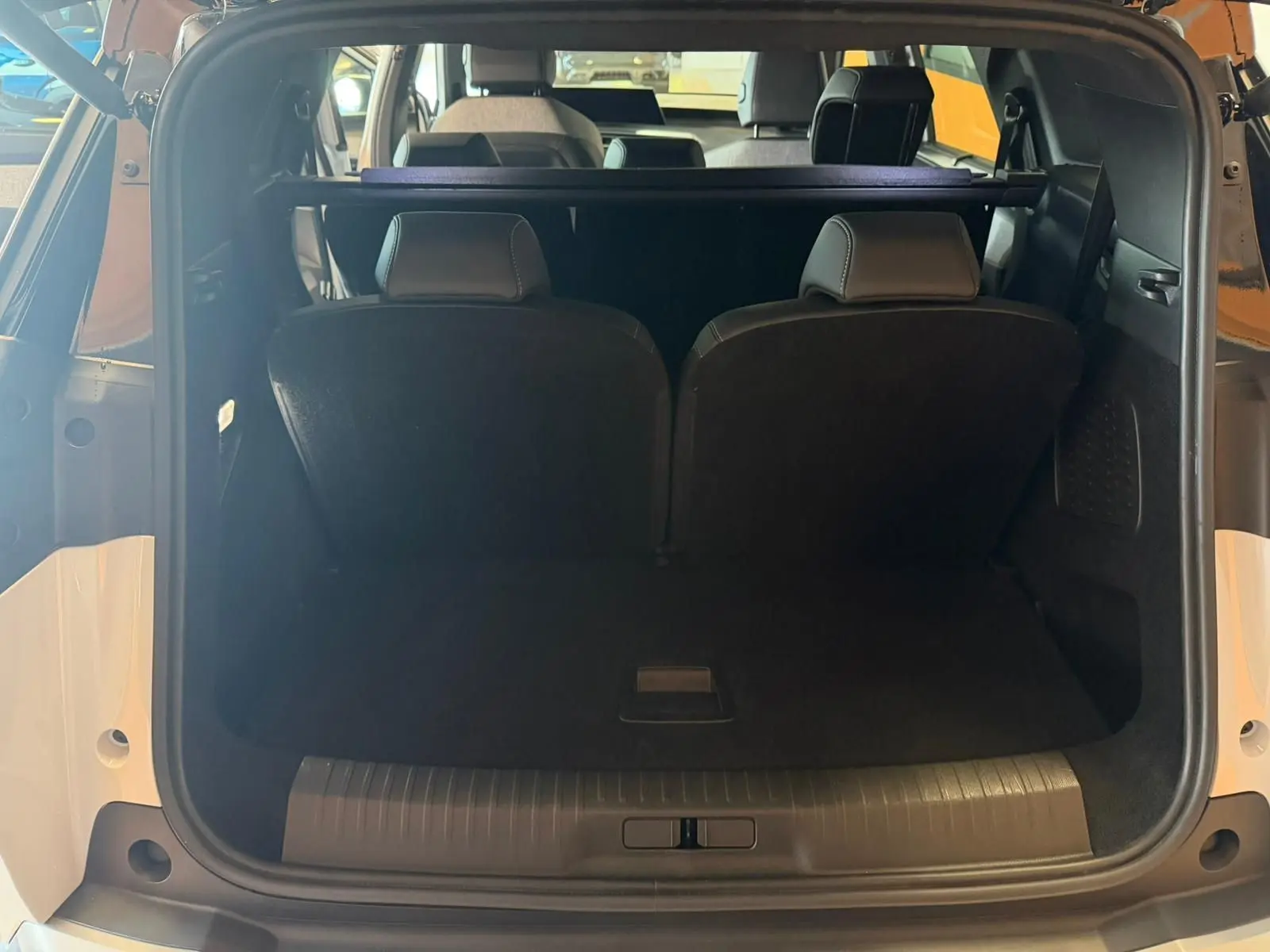 Vue arrière du coffre ouvert du Peugeot 5008 Hybrid blanc Okenite, montrant les sièges arrière et l'espace de chargement.
