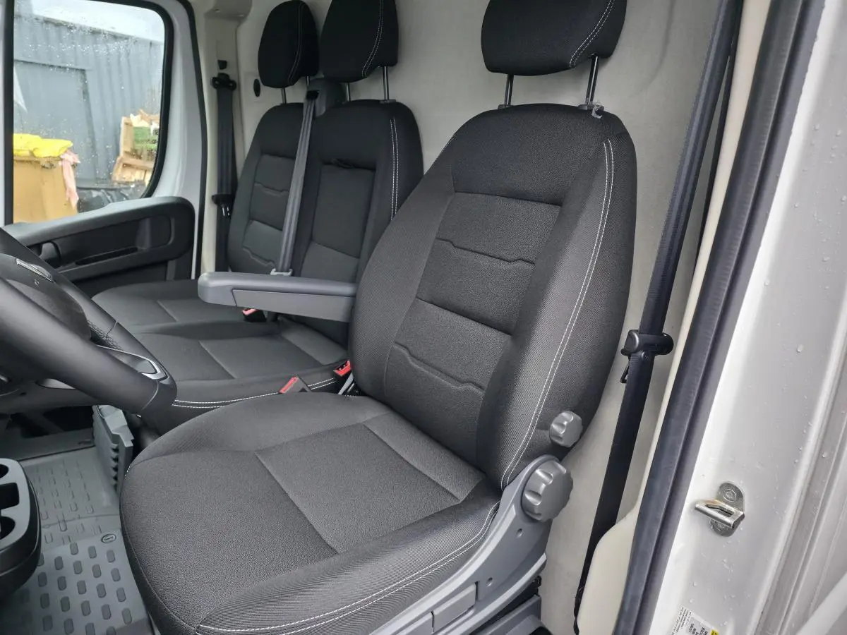 Vue intérieure côté conducteur du Peugeot Boxer Fourgon 2025, sièges tissu noir avec accoudoir et ceintures visibles.