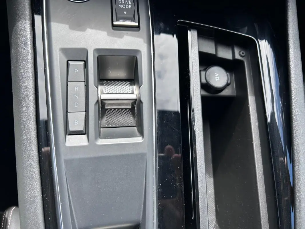 Gros plan sur la console centrale noire de la Peugeot 508 Hybrid 225 e-EAT8 avec sélecteur de boîte auto et prise 12V.