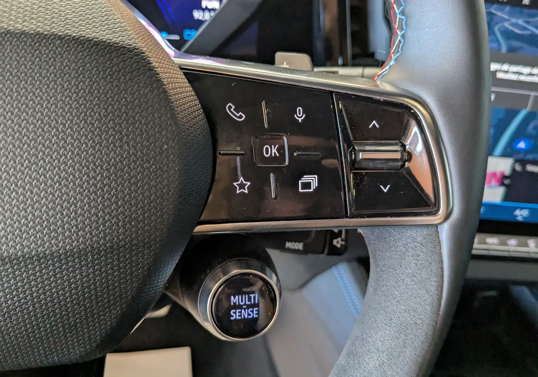 Gros plan sur les commandes gauche du volant noir de la Renault Espace VI E-Tech, avec bouton Multi Sense et surpiqûres bleues.
