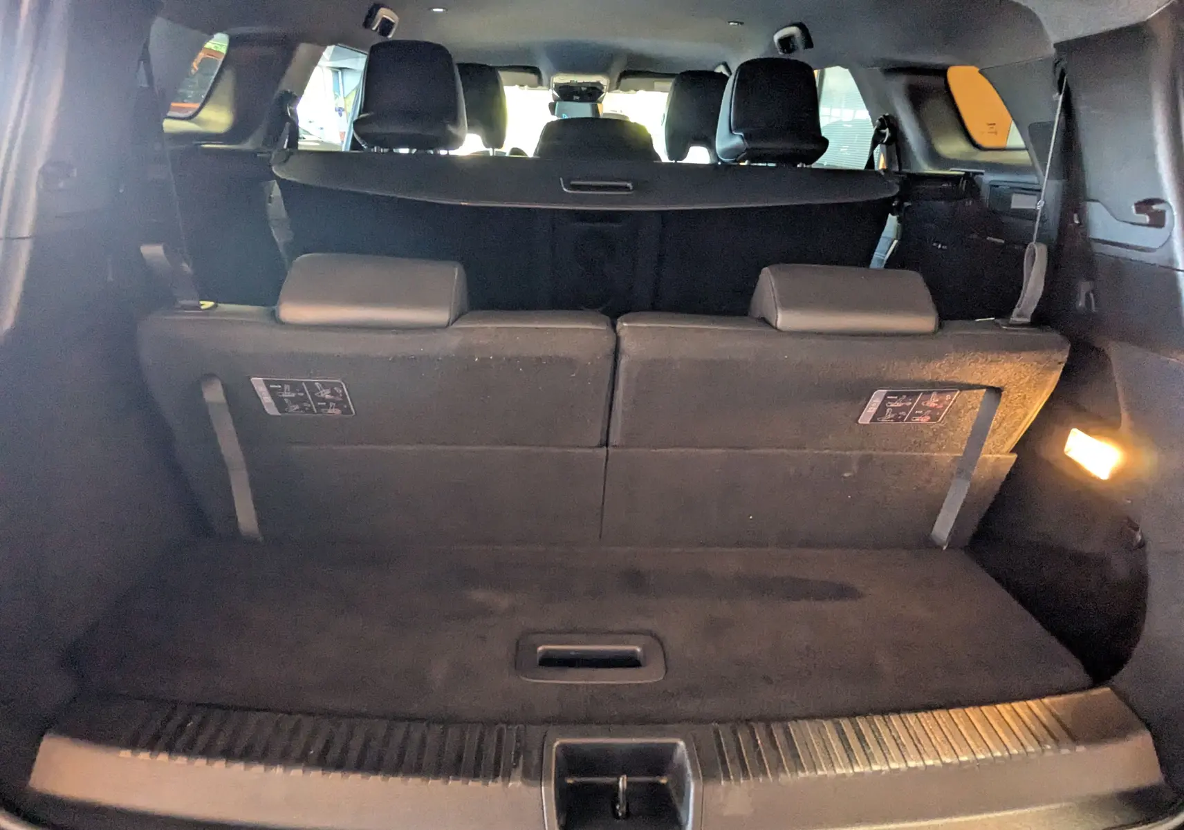 Vue depuis le coffre du Renault Espace VI noir étoile, montrant la banquette arrière relevée et l'éclairage intérieur allumé.