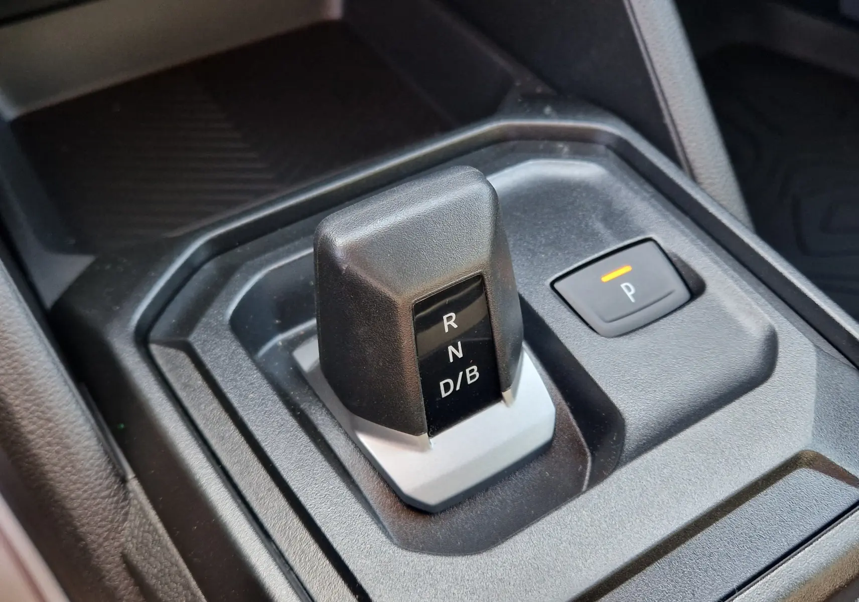 Gros plan sur le levier de vitesses automatique noir et gris du Dacia Duster 1.8 Hybrid 155, avec bouton de parking éclairé.