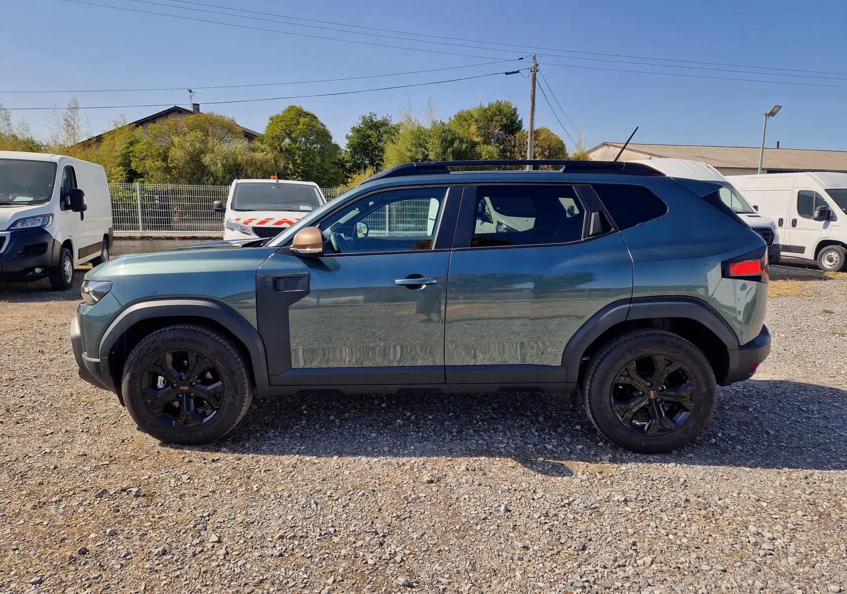 Vue de profil côté gauche d'un Dacia Duster 1.8 Hybrid 155 Extreme vert cèdre avec jantes noires et rétroviseurs bronze.