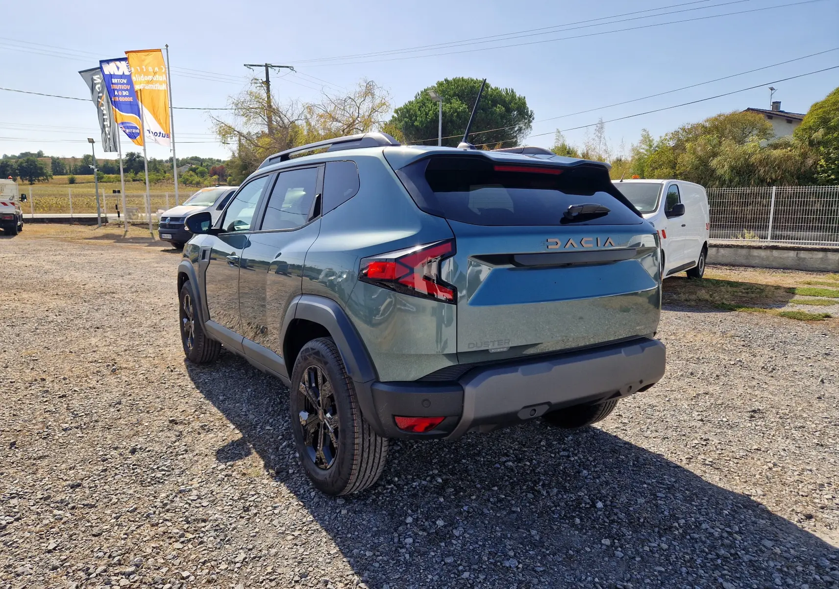 Vue 3/4 arrière droite du Dacia Duster 1.8 Hybrid 155 Extreme vert cèdre avec jantes noires et barres de toit.