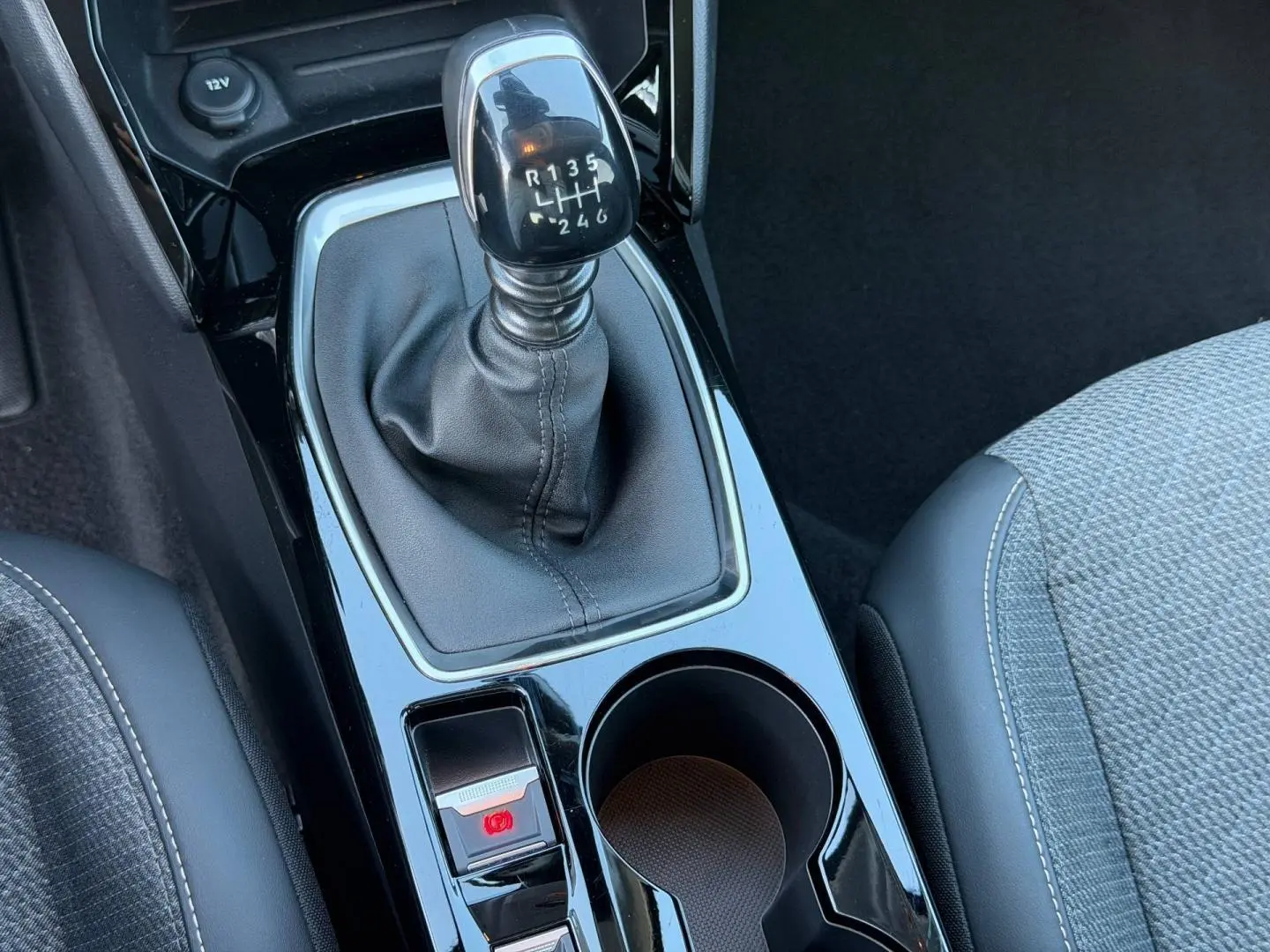 Gros plan sur la console centrale de la Peugeot 208 2025, avec levier de vitesse manuel et sellerie tissu gris.