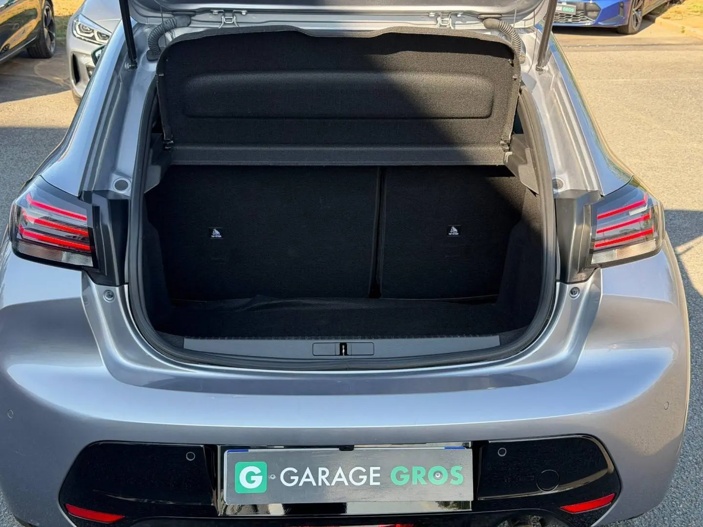 Coffre ouvert vu de l'arrière d'une Peugeot 208 1.2 100ch gris Artense avec feux arrière LED distinctifs.