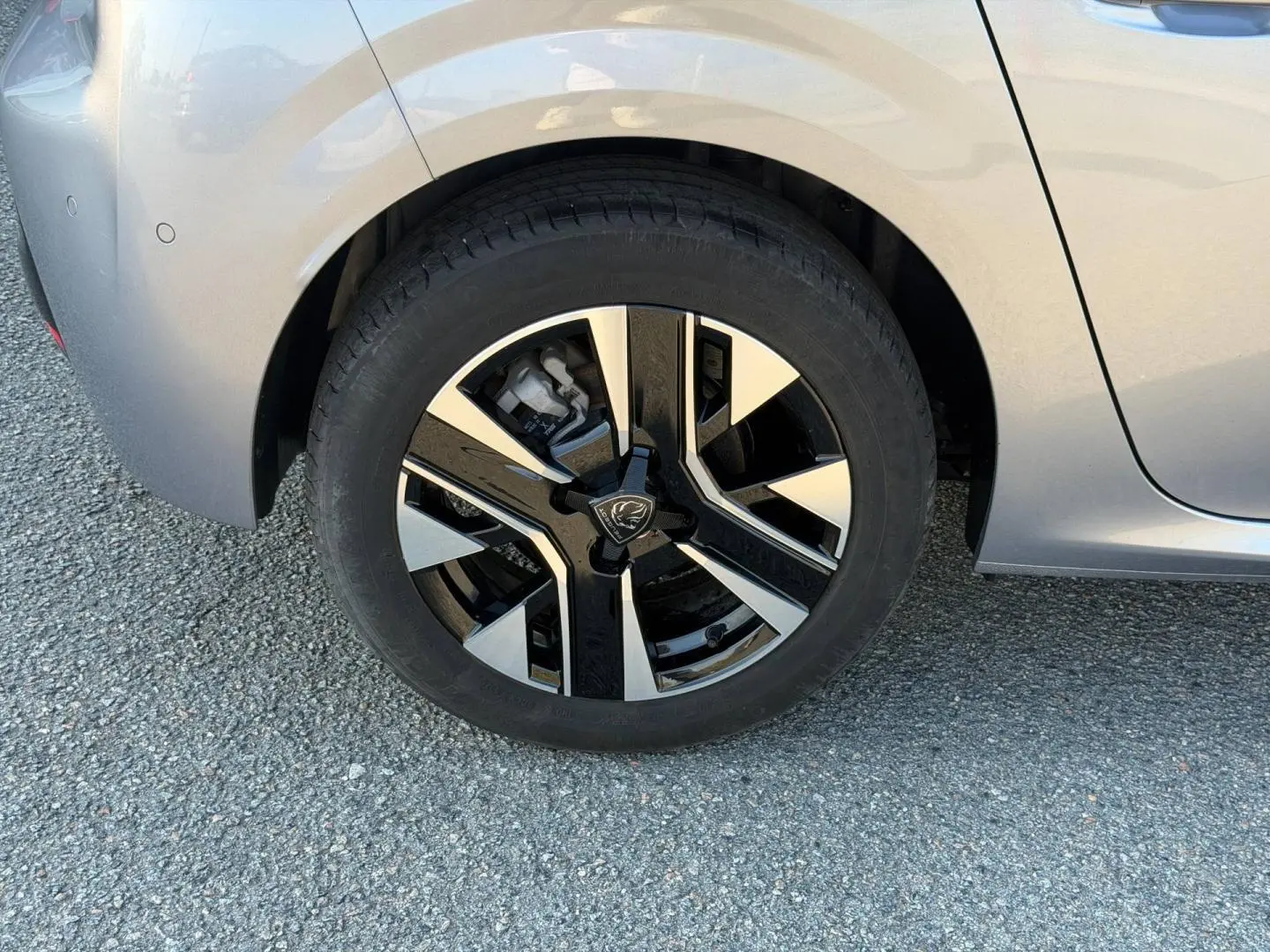 Gros plan sur la roue avant gauche d'une Peugeot 208 gris Artense avec jante alu bicolore moderne.