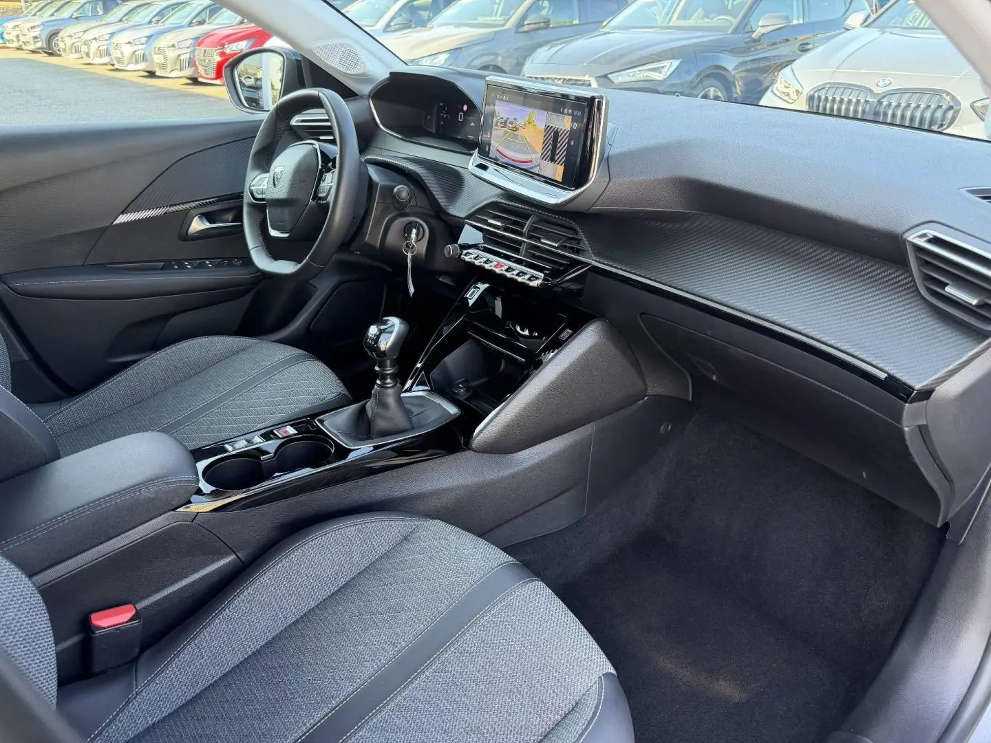 Vue intérieure côté conducteur de la Peugeot 208 1.2 100ch 2025, montrant la console centrale avec boîte manuelle et écran tactile.
