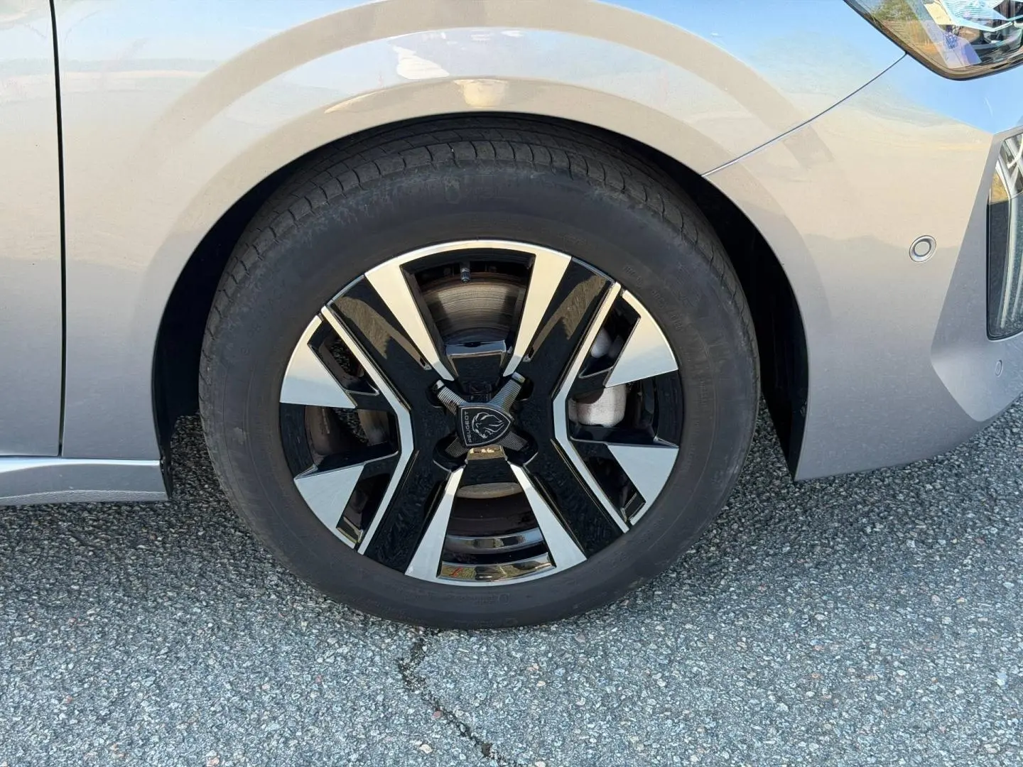 Gros plan sur la roue avant gauche d'une Peugeot 208 gris Artense avec jante alliage bicolore moderne.