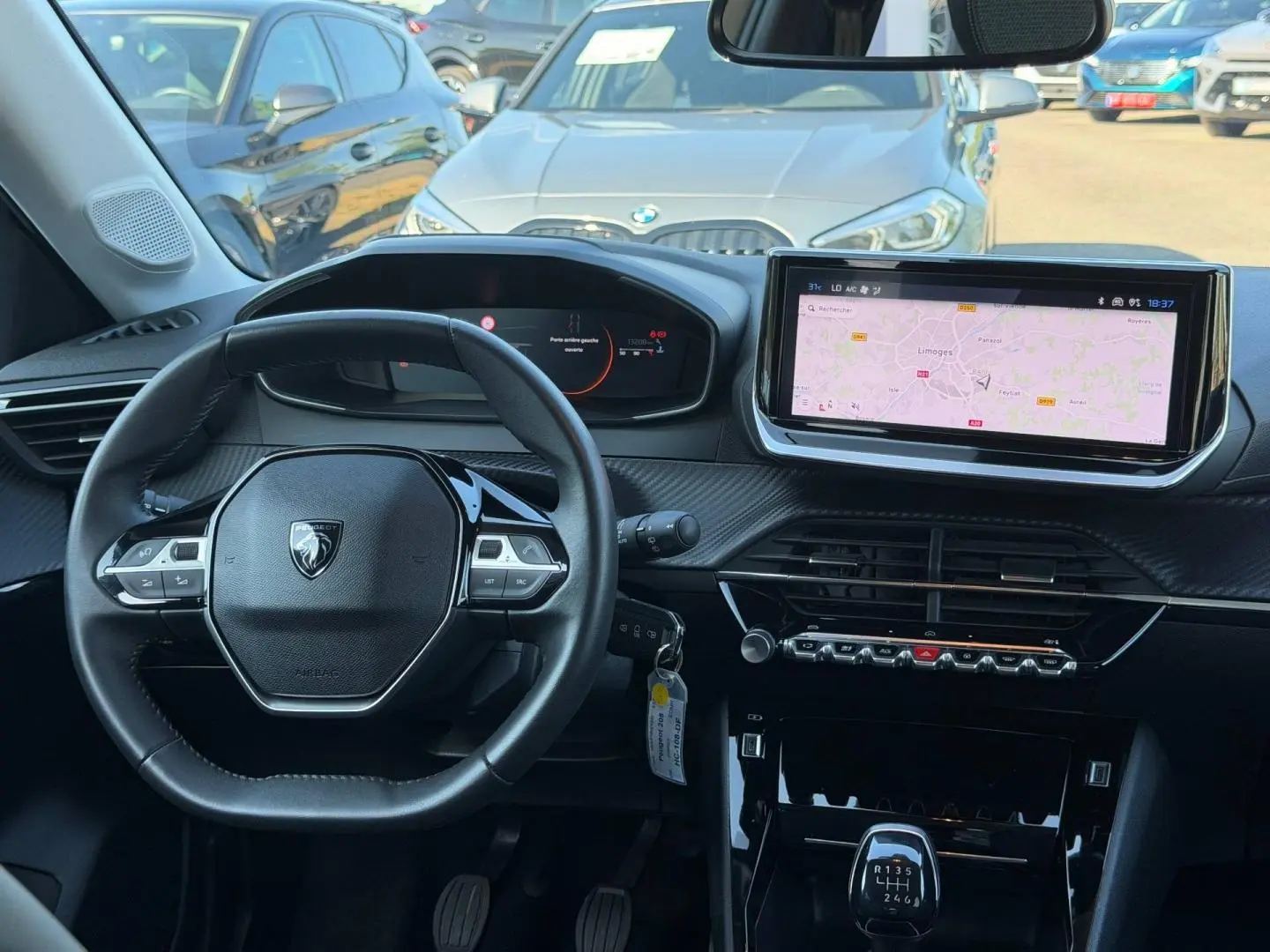 Vue intérieure frontale du tableau de bord et volant noir du Peugeot 208 1.2 100ch avec écran tactile et boîte manuelle.