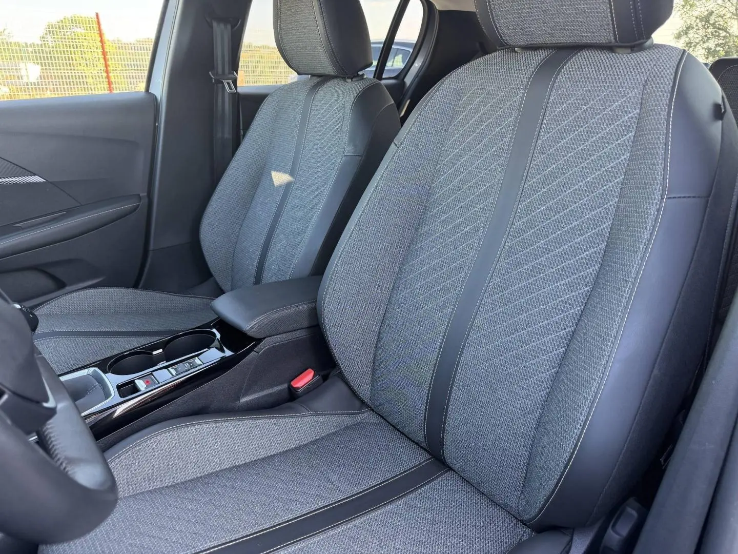 Vue intérieure côté conducteur de la Peugeot 208 1.2 100ch gris Artense, sièges tissu gris avec surpiqûres noires.