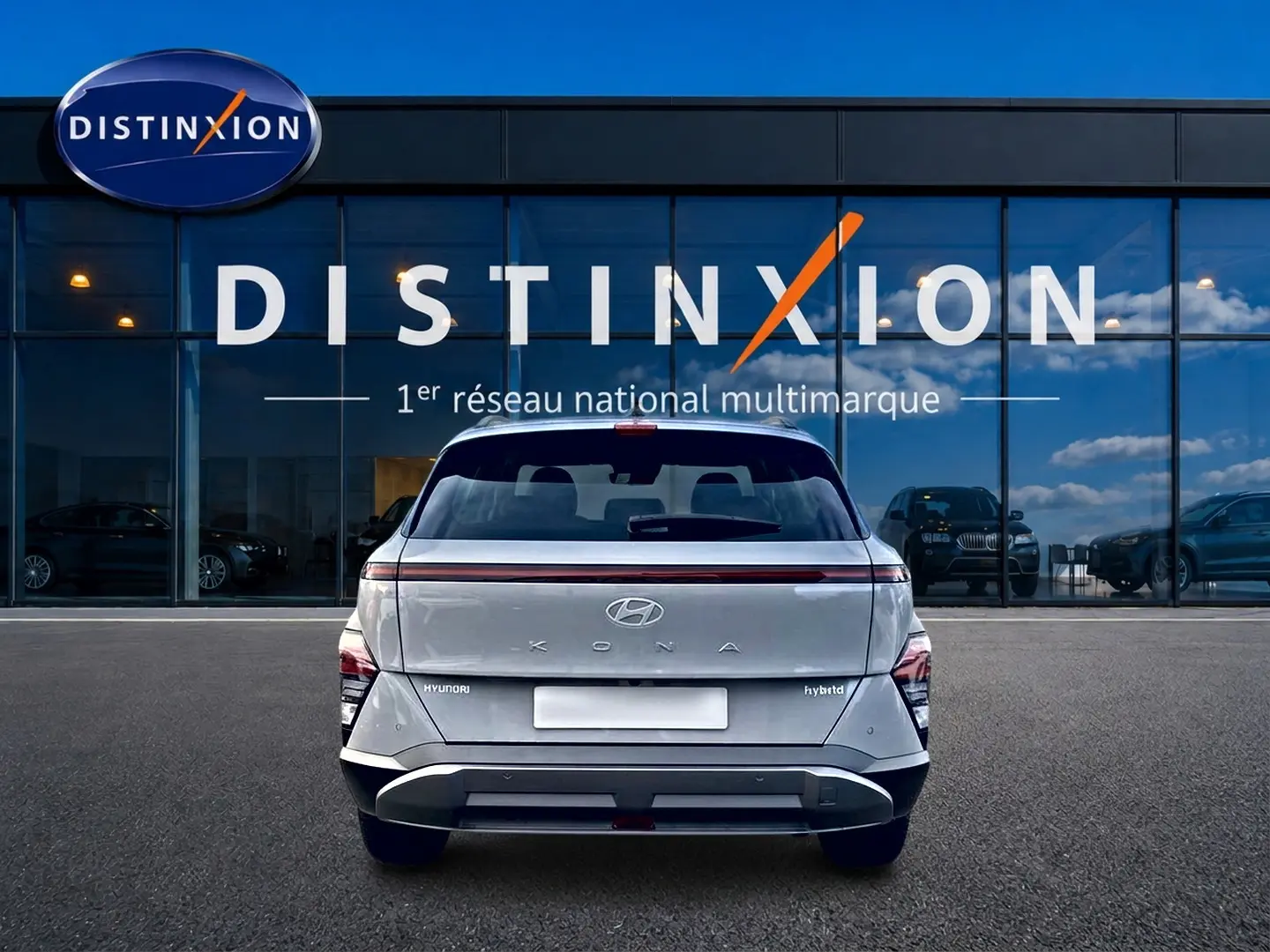 Vue arrière d'un Hyundai Kona gris 2025 hybride, avec feux arrière à LED et logo distinctif sur fond de vitrine Distinxion.