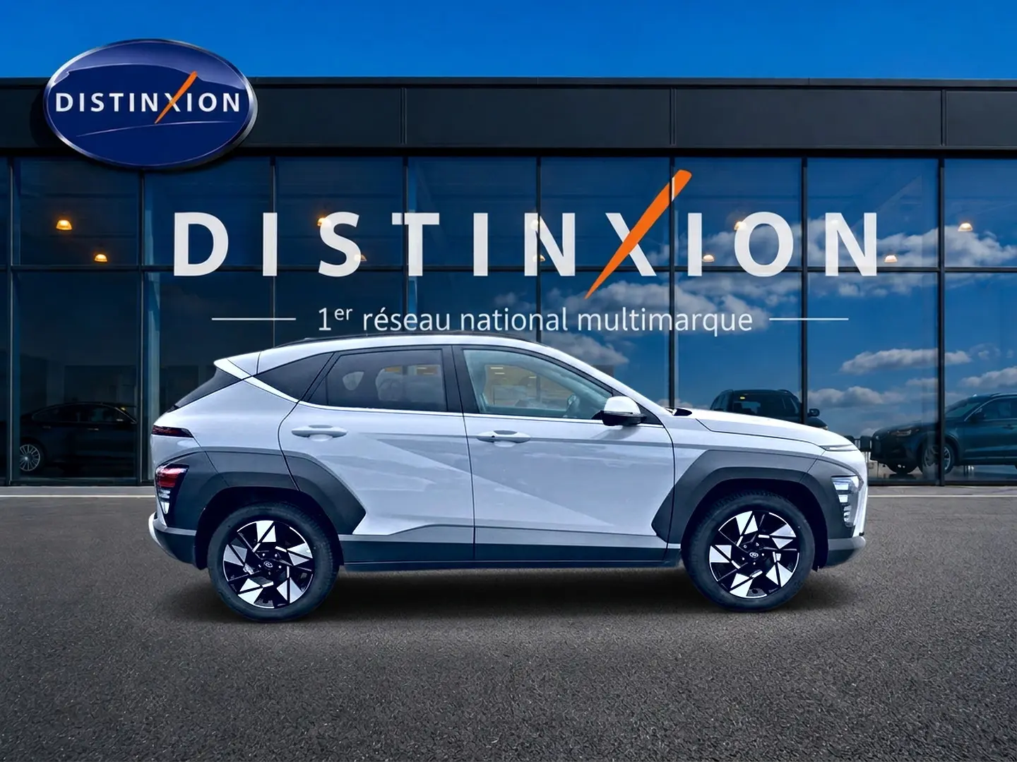 Vue latérale droite d'un Hyundai Kona gris 2025 avec protections noires et jantes alliage bicolores devant une vitrine Distinxion.