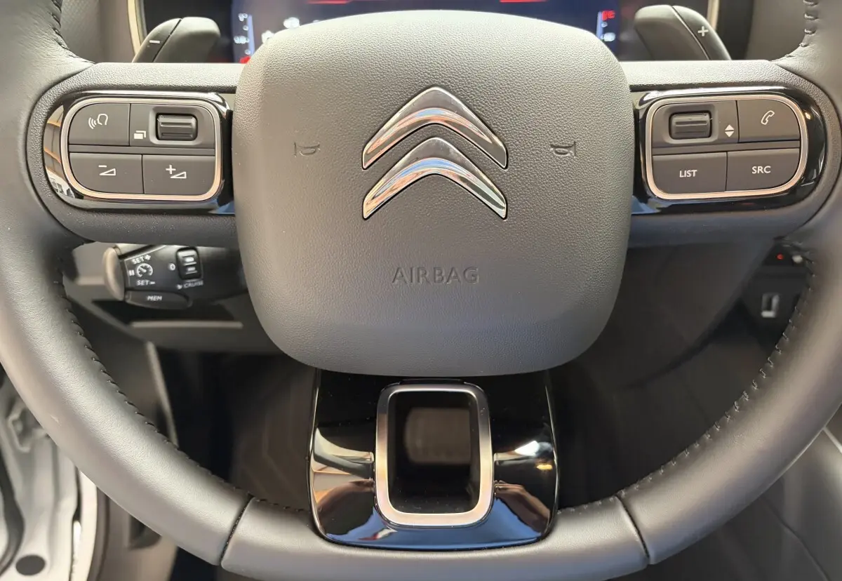 Gros plan sur le volant cuir noir du Citroën C5 Aircross 2025 avec commandes multifonctions et logo chromé central.