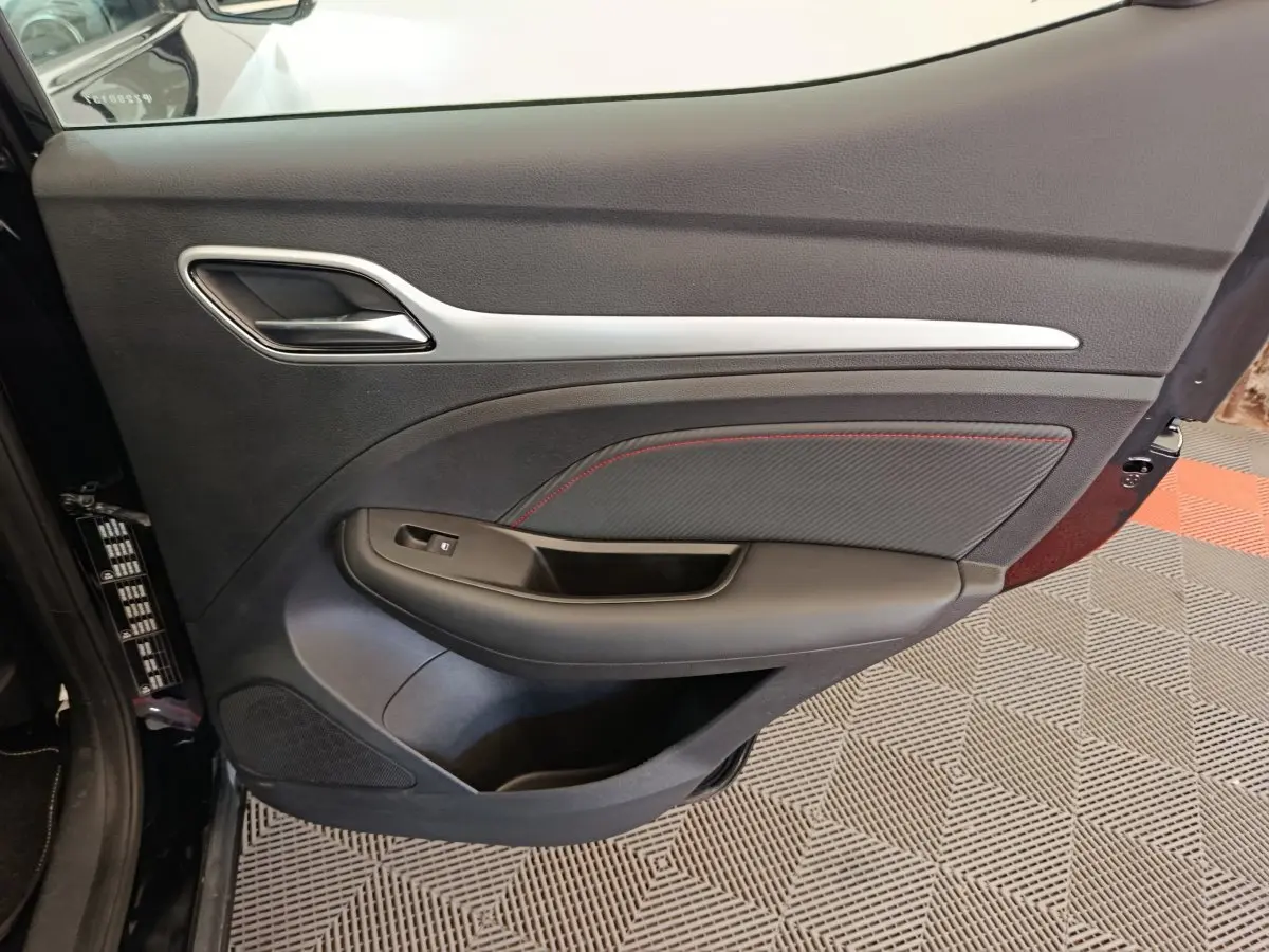 Vue côté intérieur de la porte avant gauche du MG ZS Luxury noir, avec surpiqûres rouges et poignée chromée.