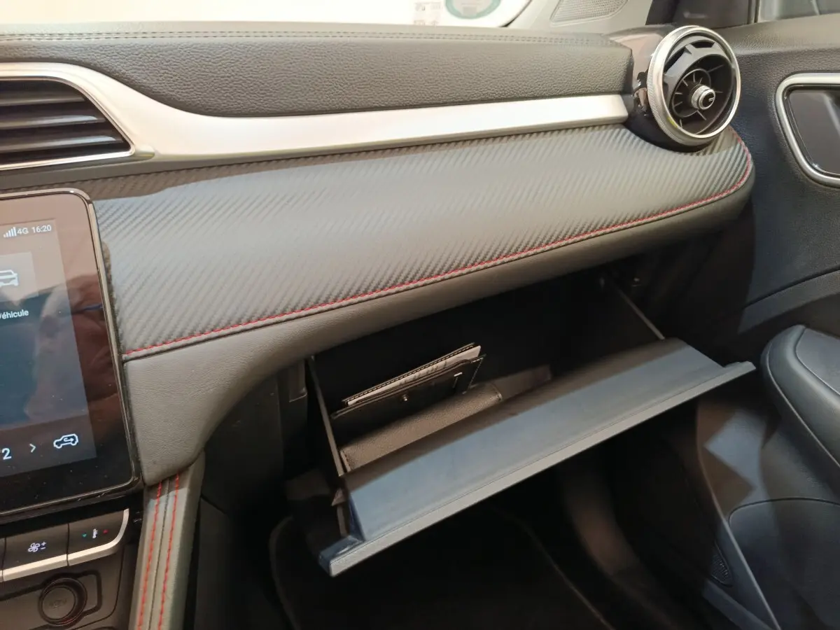 Intérieur côté passager du MG ZS Luxury 2024, tableau de bord gris avec surpiqûres rouges et boîte à gants ouverte.