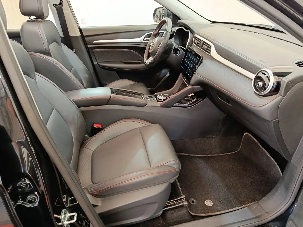 Vue intérieure côté conducteur du MG Motor ZS Luxury 70kWh 2024 noir, sièges cuir avec surpiqûres rouges et écran tactile central.