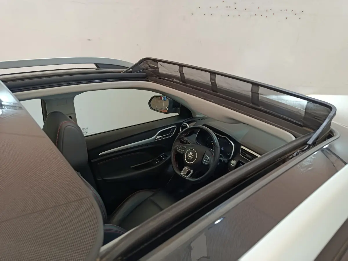 Vue intérieure par le toit ouvrant du MG Motor ZS Luxury 70kWh 2024 noir, volant cuir multifonctions et sièges noirs.