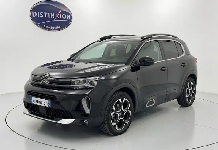 Vue 3/4 avant d'un Citroën C5 Aircross hybride noir 2024 avec jantes distinctives et barres de toit visibles.